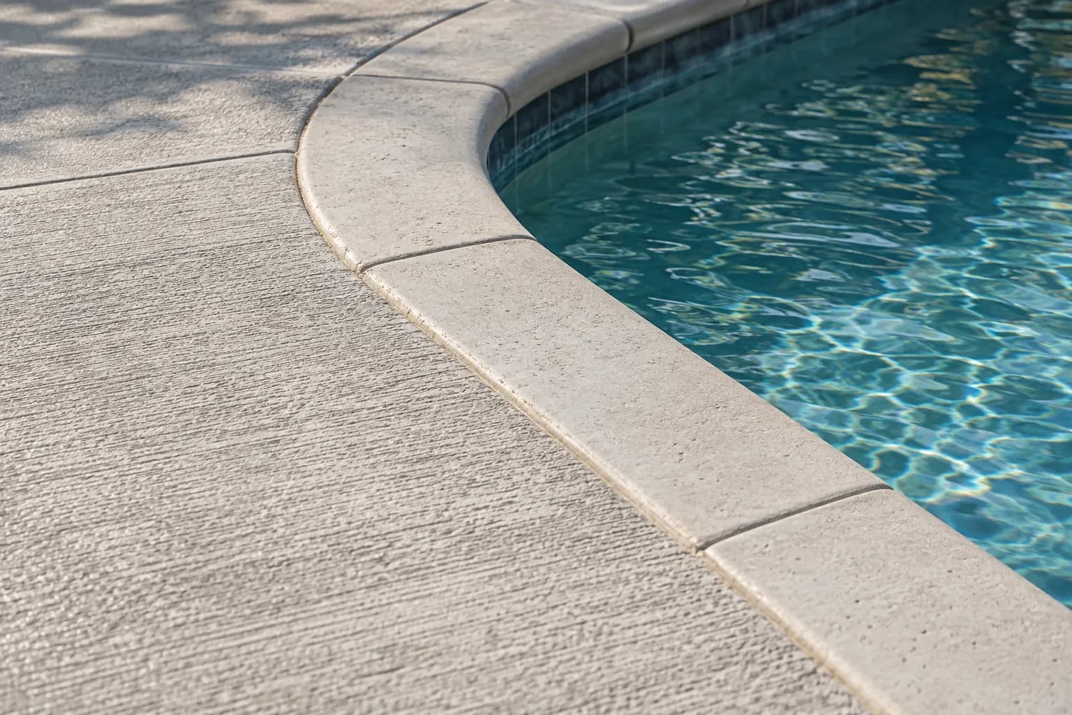 Light concrete pool deck with a non-slip texture beside the coping