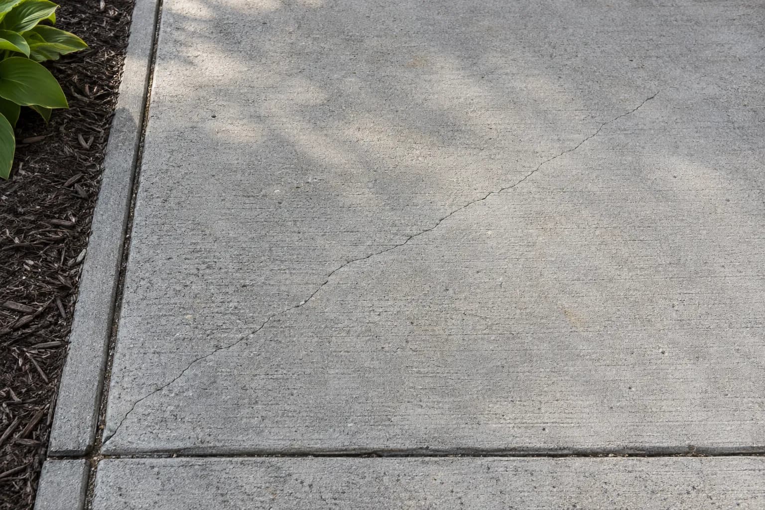Thin shrinkage crack running across a concrete driveway panel